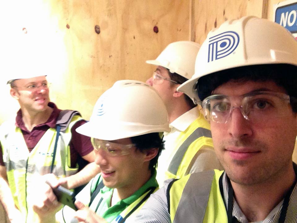 Members of the floored team, bedecked in hard hats and high visibilty vests, inside a plywood elevator.